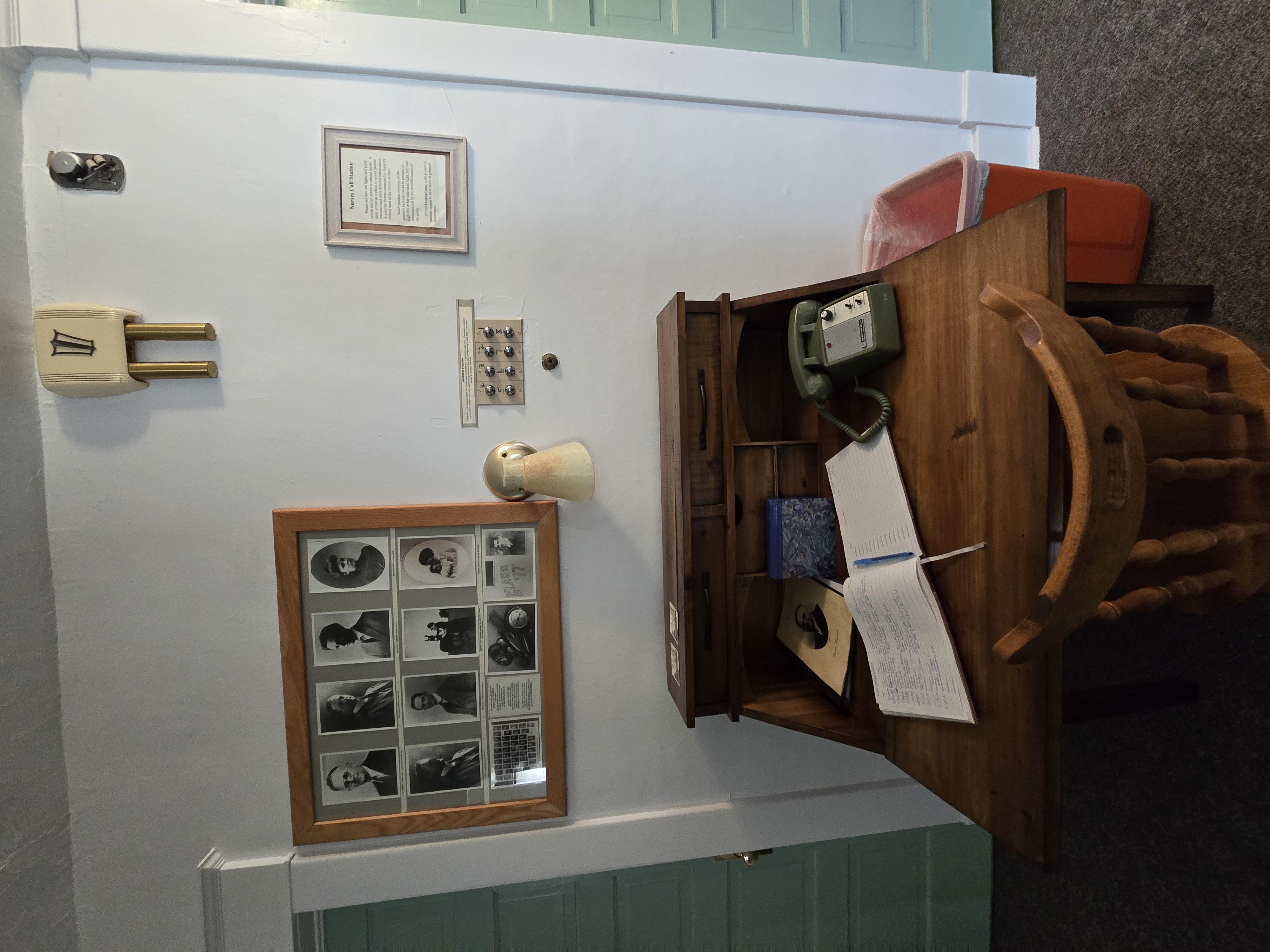 Wooden desk and chair, green telephone, notebook, wood frame black and white photos, 8 call buttons, chime door bell