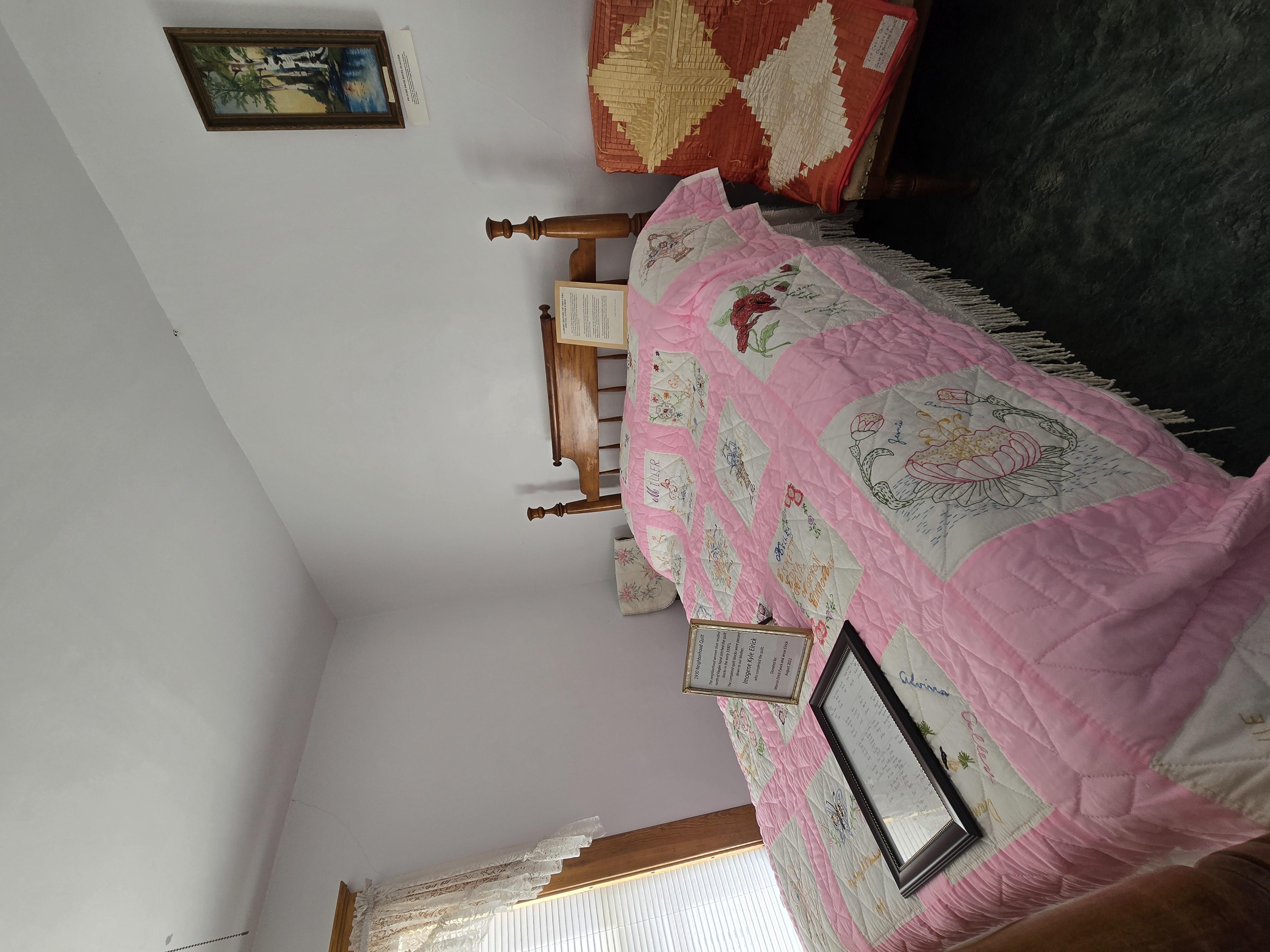 Wood bed, pink and white quilt, red, yellow and white quilt, picture on the wall of palm tree by water