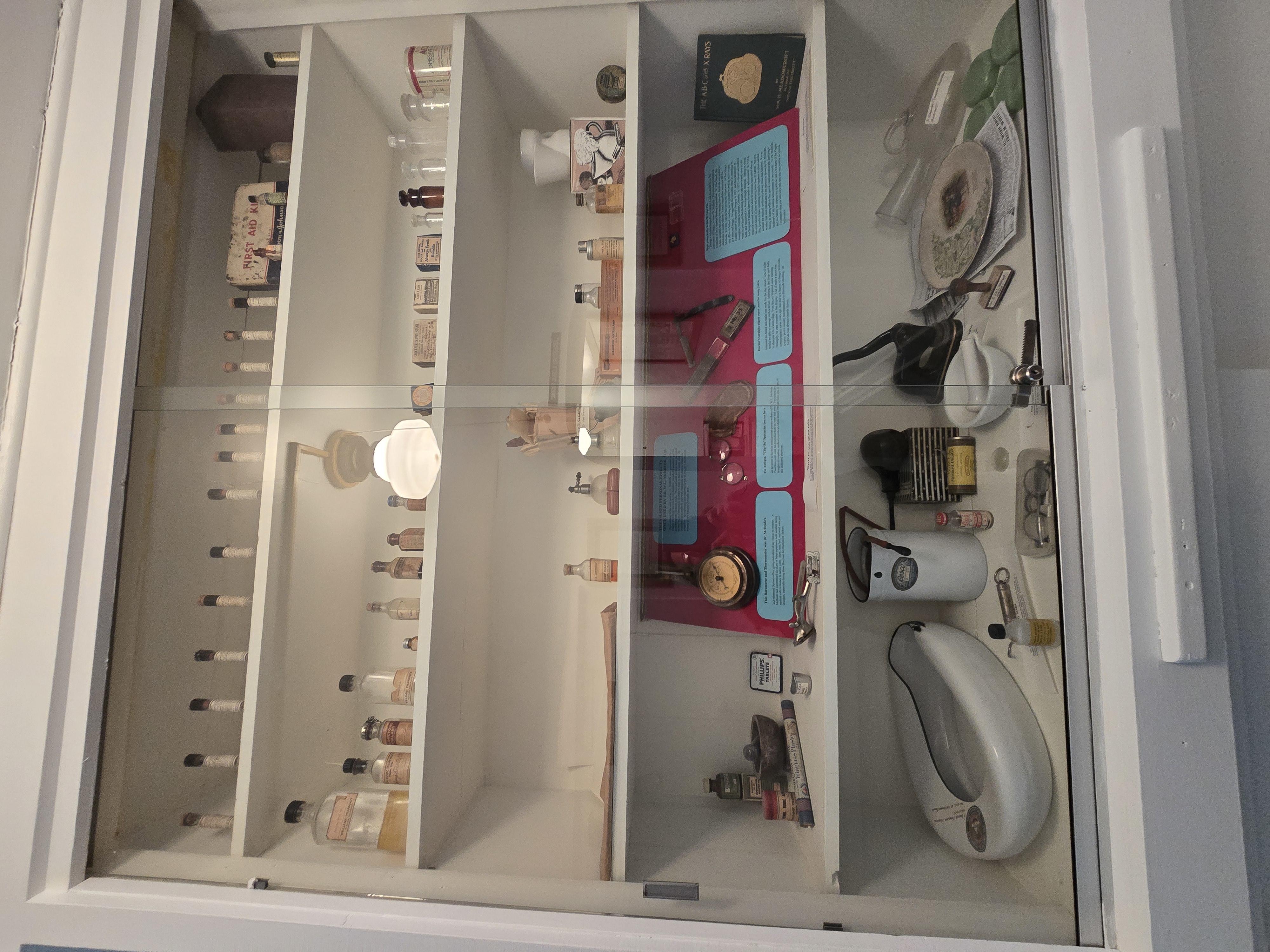 Glass display of glass medicine bottles, white metal bed pan