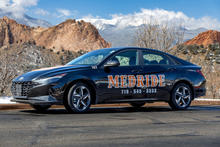 Black vehicle with orange and white lettering, on road with mountains and sky 